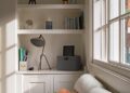 Cozy home office nook with shelves, desk lamp, and decorative items by the window.