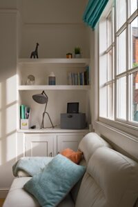 Cozy home office nook with shelves, desk lamp, and decorative items by the window.