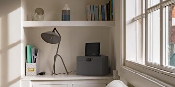 Cozy home office nook with shelves, desk lamp, and decorative items by the window.