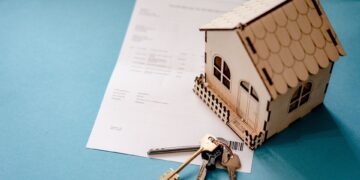 Small wooden house model with keys and documents on blue background.