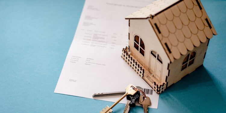 Small wooden house model with keys and documents on blue background.