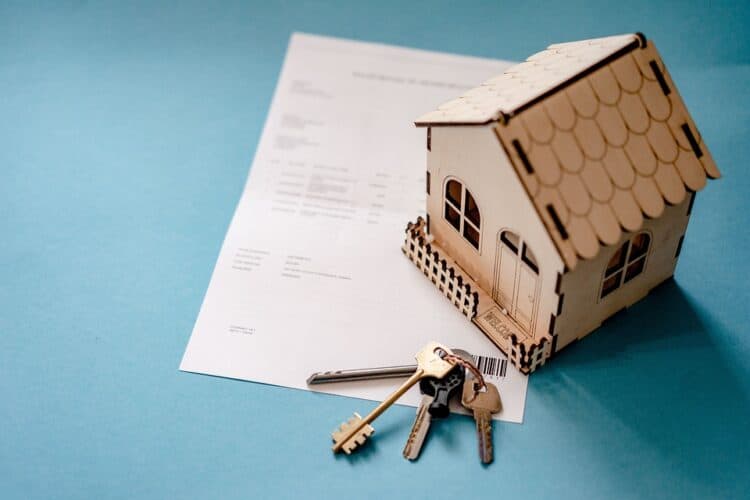 Small wooden house model with keys and documents on blue background.