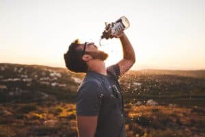 Man drinking from a bottle outdoors at sunset, symbolizing innovation and boldness.